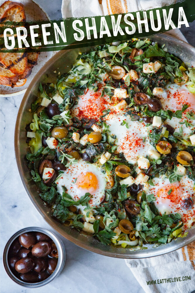 A pan of green Shakshuka with a plate of toast and a small bowl of ripe olives next to it.