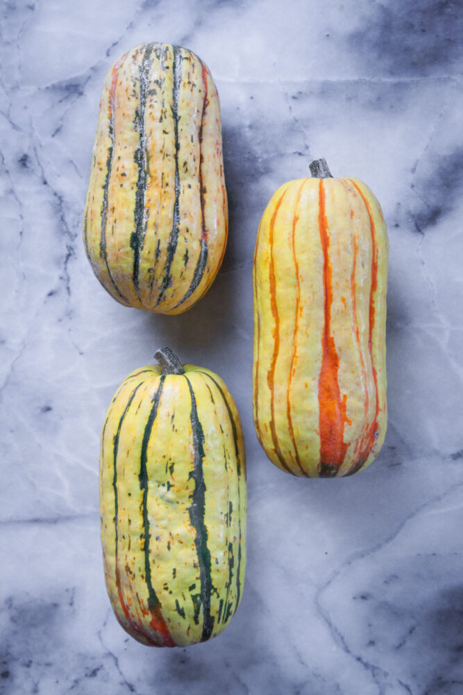 Three Delicata squash on a marble surface.