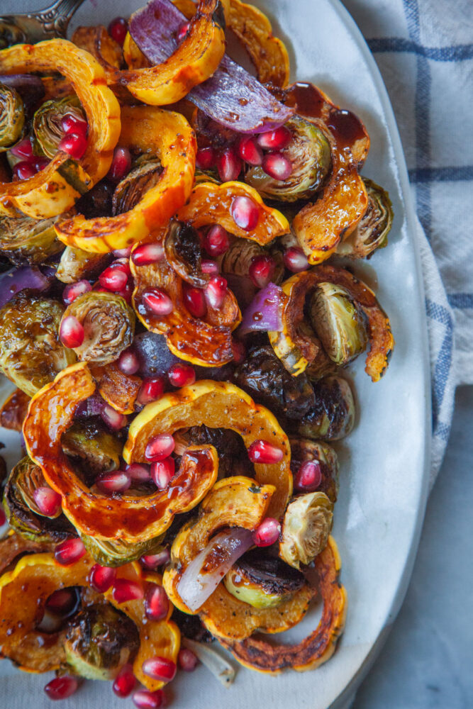 A plate with roasted Delicata squash and Brussels sprouts with pomegranate agrodolce drizzled over it.