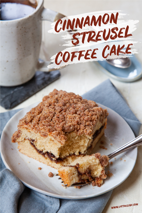 A piece of cinnamon streusel coffee cake on a small plate, with a mug of tea behind it.