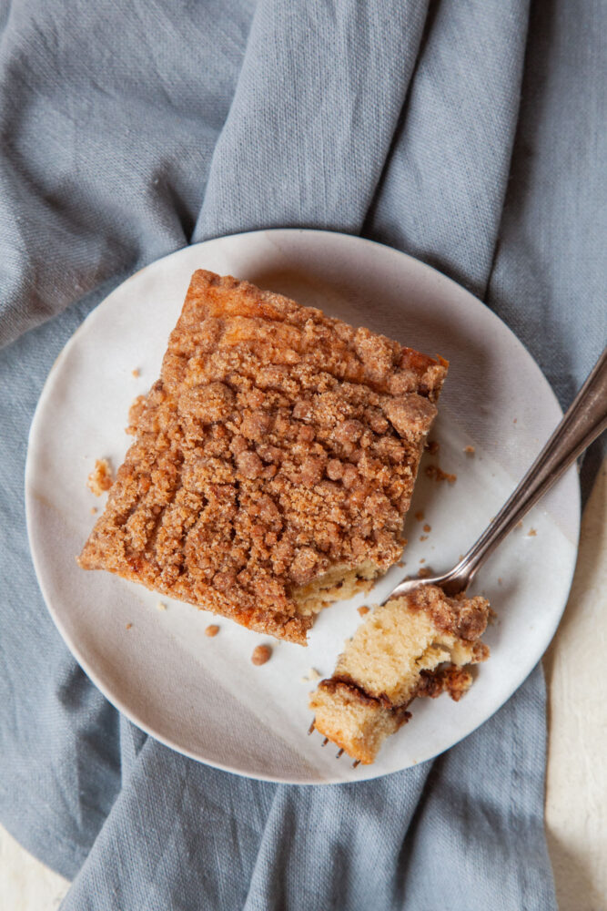A slice of cinnamon streusel coffee cake with a fork having taking a piece out of it on a small plate.