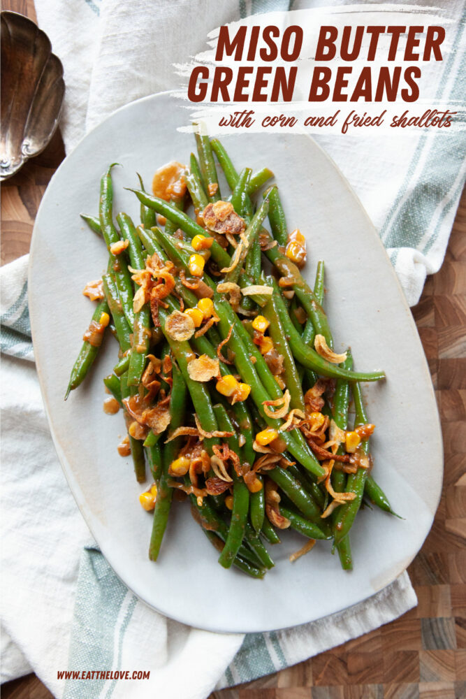 An oval plate with miso butter glazed green beans with corn and fried shallots on it.