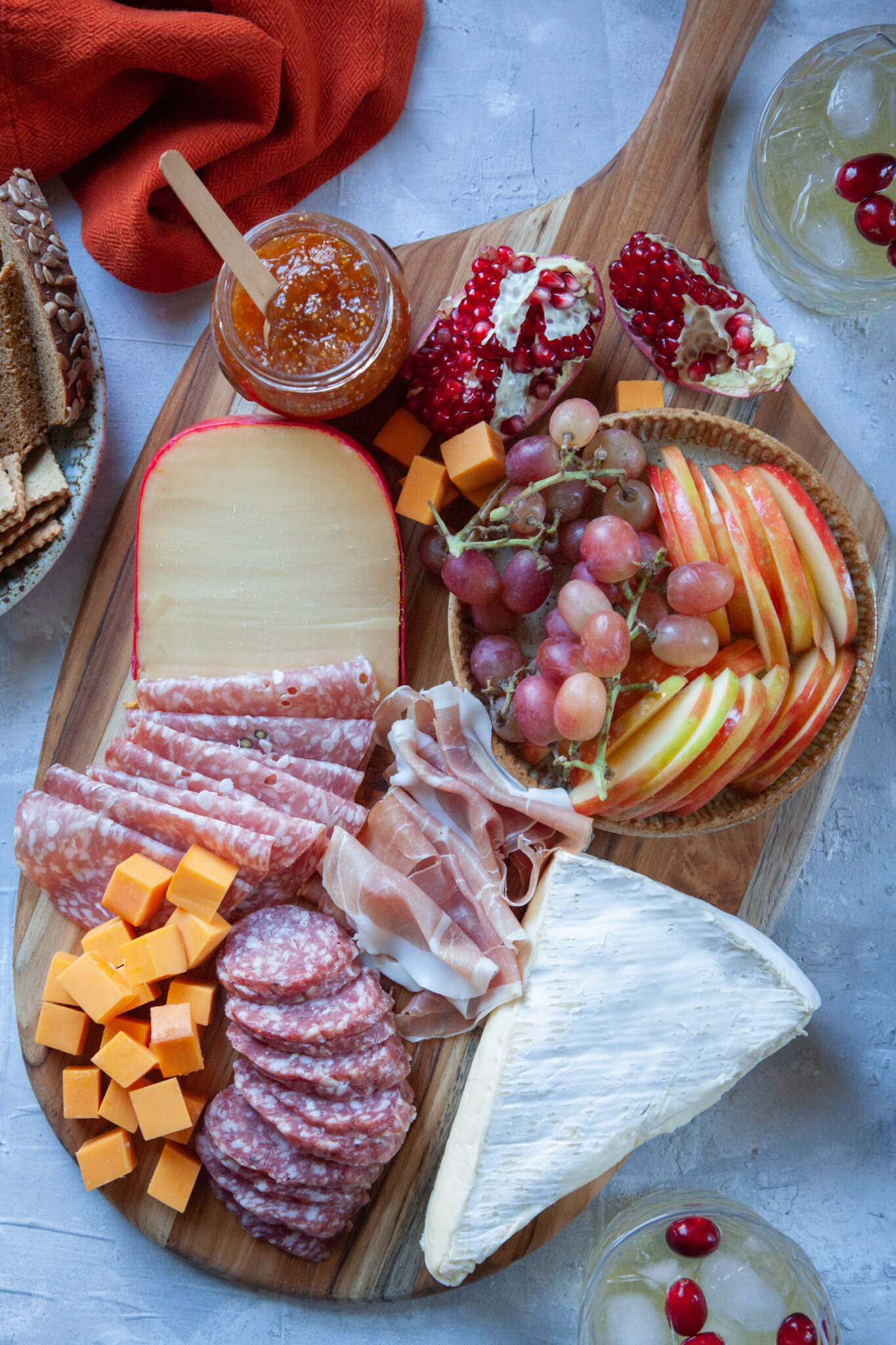 A holiday charcuterie board with cheese, charcuterie, fruit, jam crackers and bread, with a holiday cocktail next to the board.