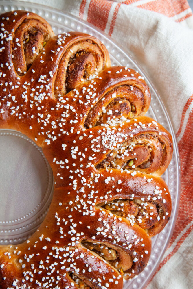 A Swedish Tea Ring on a glass plate, with a orange and white striped cloth napkin under the plate.