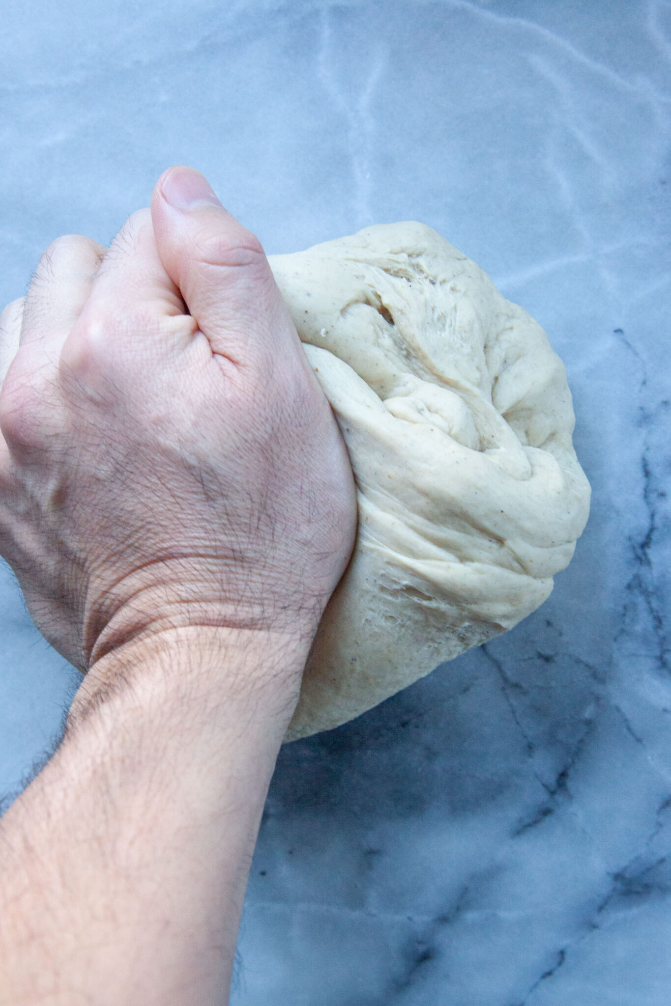 A hand kneading dough on a marble surface.