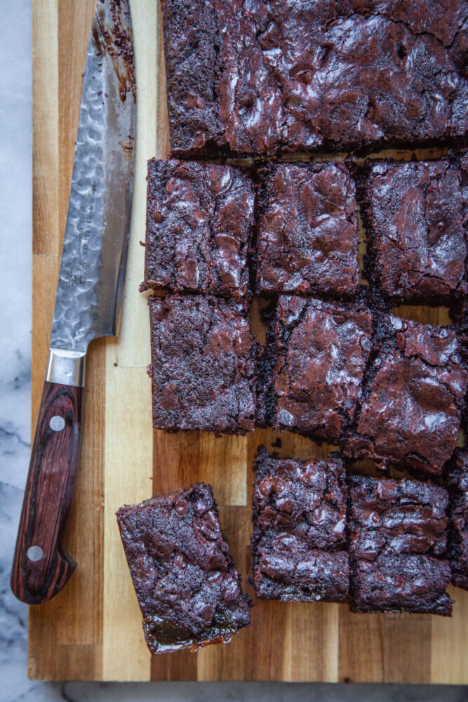 Miso caramel soy sauce brownies on a cutting board, cut into small rectangles, with a small utility knife next to the brownies.