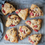 Chocolate and strawberry scones on a wire cooling rack. The rack is sitting on a marble surface. There is a blue cloth napkin next to the cooling rack and scones.