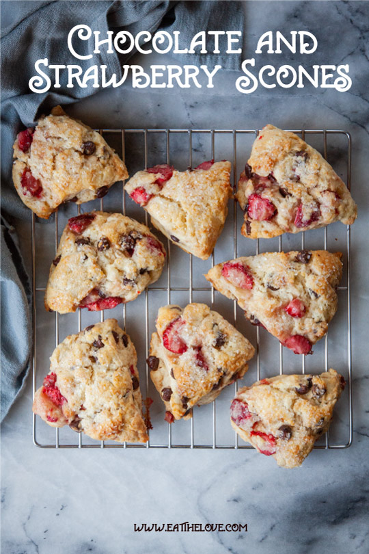 Chocolate and strawberry scones on a wire cooling rack. The rack is sitting on a marble surface. There is a blue cloth napkin next to the cooling rack and scones.