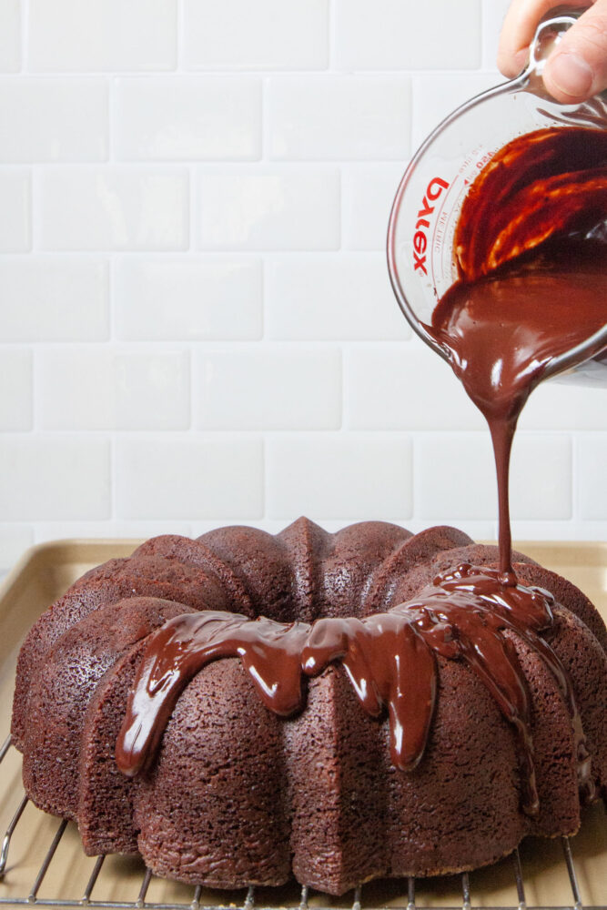 Chocolate ganache being drizzled onto a bundt cake from a glass measuring cup.