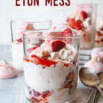 A double old fashion glass filled with British Eton Mess, a strawberry, meringue and whipped cream dessert. There are more glasses of Eton Mess behind the front one.