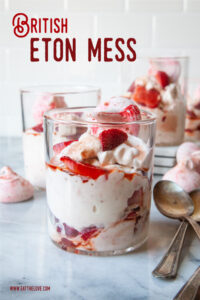 A double old fashion glass filled with British Eton Mess, a strawberry, meringue and whipped cream dessert. There are more glasses of Eton Mess behind the front one.