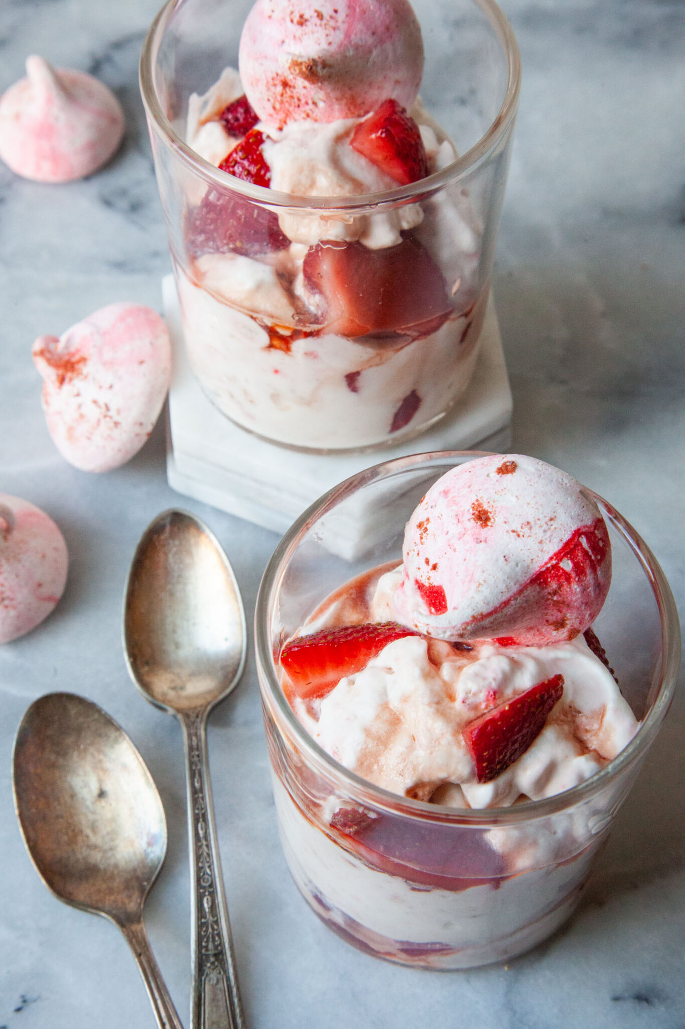 A double old fashion glass filled with British Eton Mess, a strawberry, meringue and whipped cream dessert. There are more glasses of Eton Mess behind the front one.