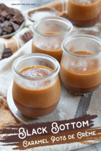 Several black bottom caramel pots de creme on a ceramic cheese board. There is a small plate of chopped chocolate chunks behind them.