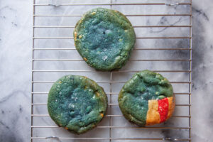 Two all blue cookies and a blue cookie with a red and white striped corner sitting on a wire cooling rack.