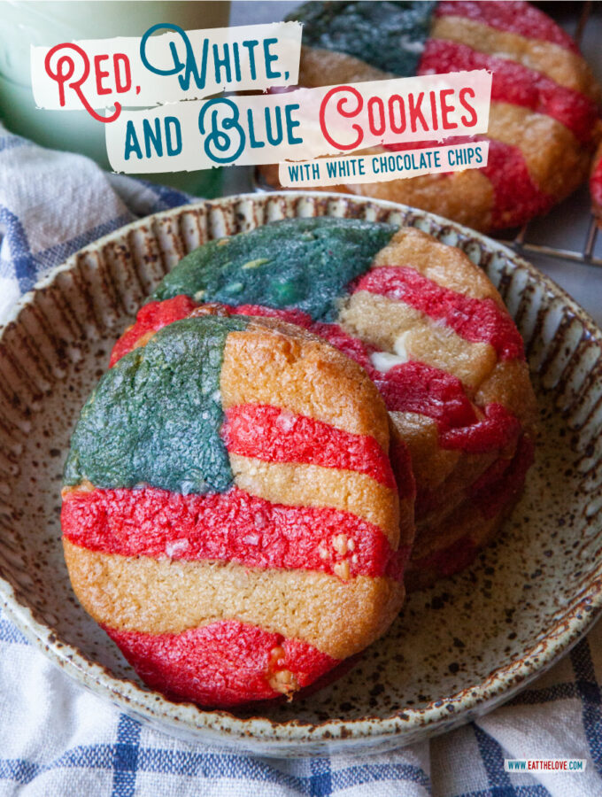 A stack of red, white, and blue American flag cookies on a plate, with a glass of milk and a wire cooling rack of more cookies behind the plate.