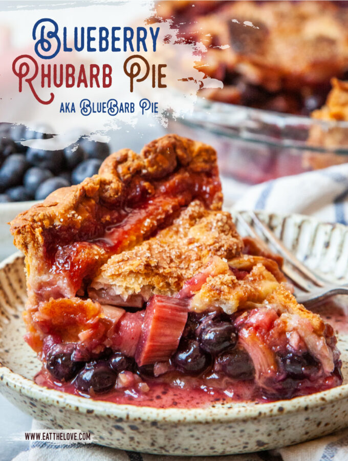 A slice of blueberry rhubarb pie on a small plate, with a bowl of blueberries and some rhubarb behind it. The remaining pie is also behind the pie slice.