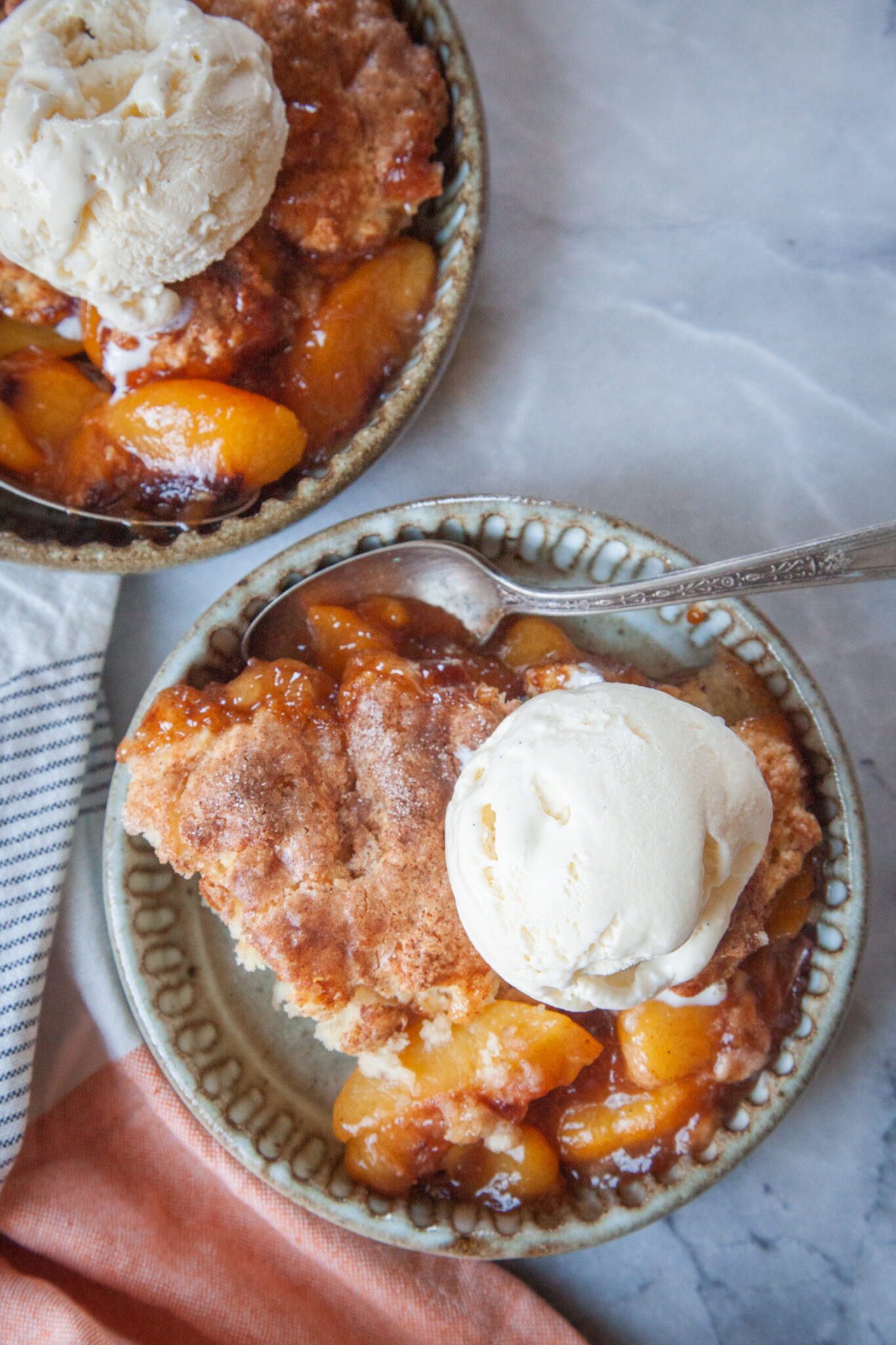 Two shallow bowls of peach cobbler with scoops of vanilla ice cream on top.
