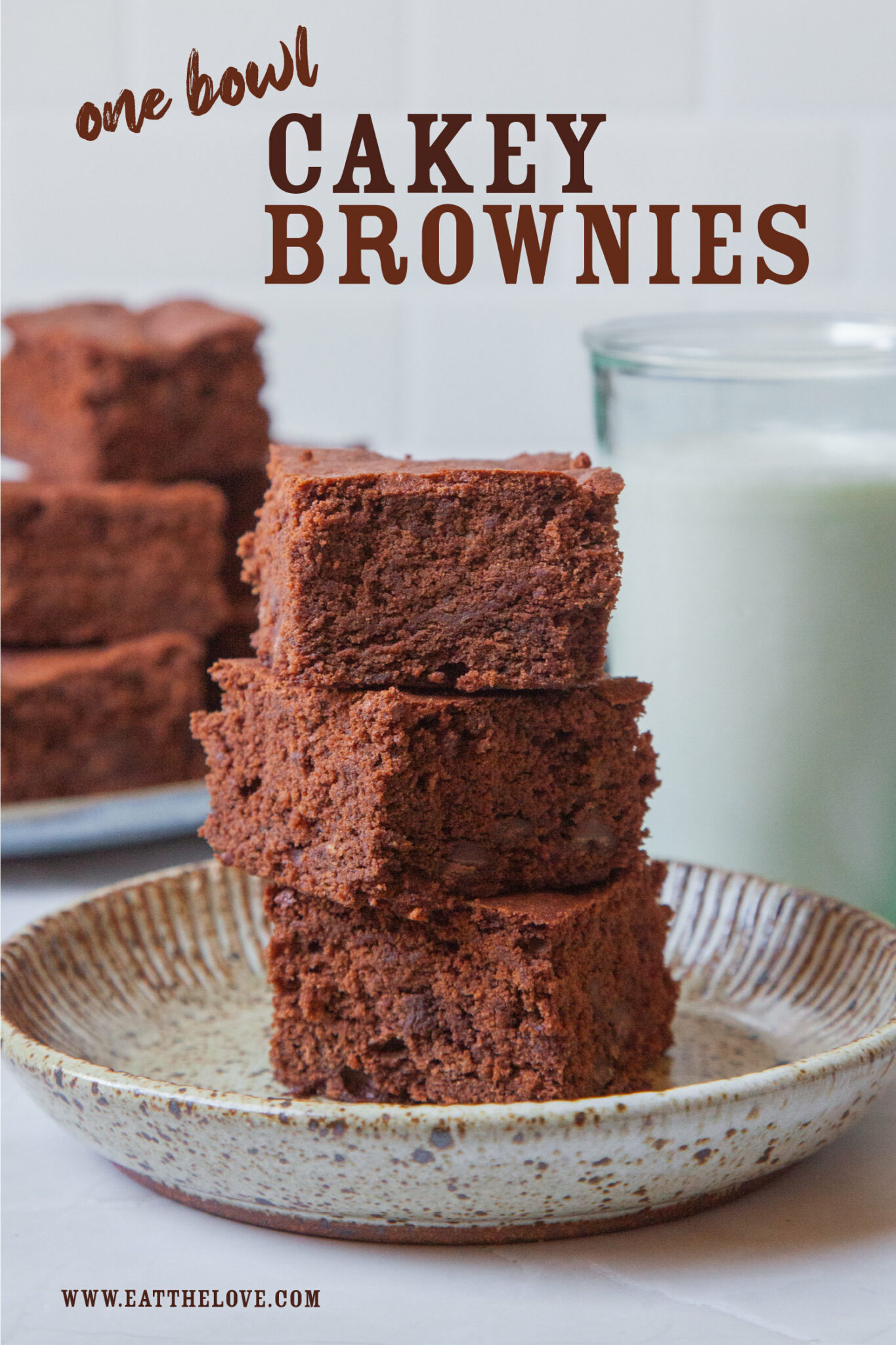 A stack of chocolate cakey brownies on a plate, with more brownies and a glass of milk behind it.