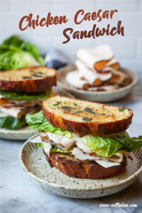 A chicken Caesar Sandwich on a plate, with another sandwich behind it. There is also a plate of sliced deli chicken behind both sandwiches. The text on the image says "Chicken Caesar Sandwich" as a headline, and in small print "www.eatthelove.com" in small print.