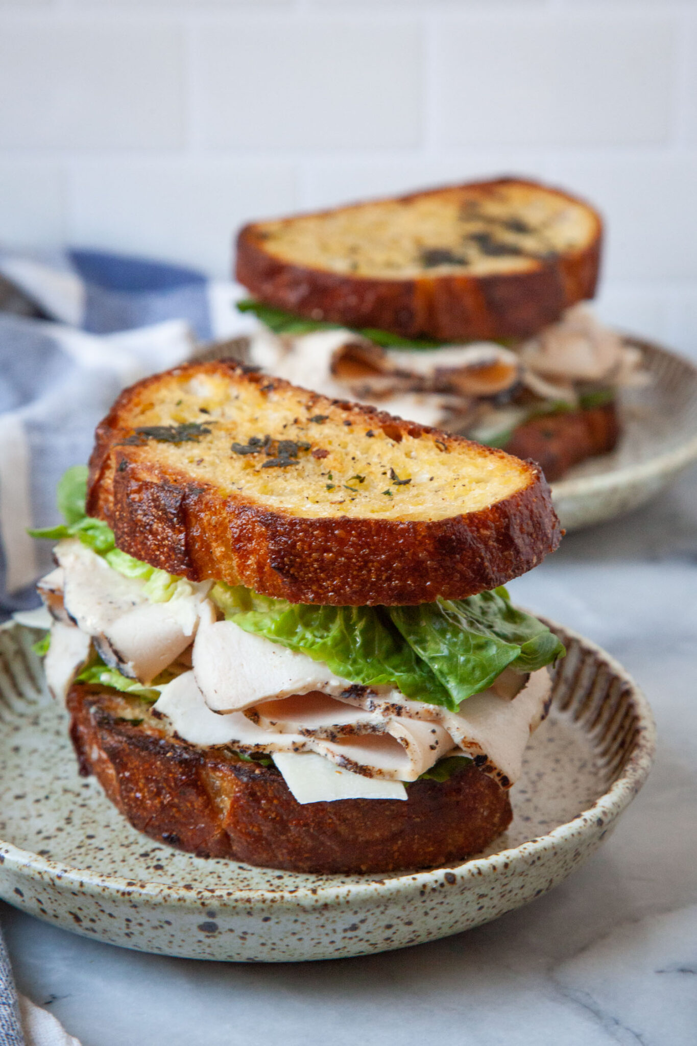 A chicken Caesar Sandwich on a plate, with another sandwich behind it.