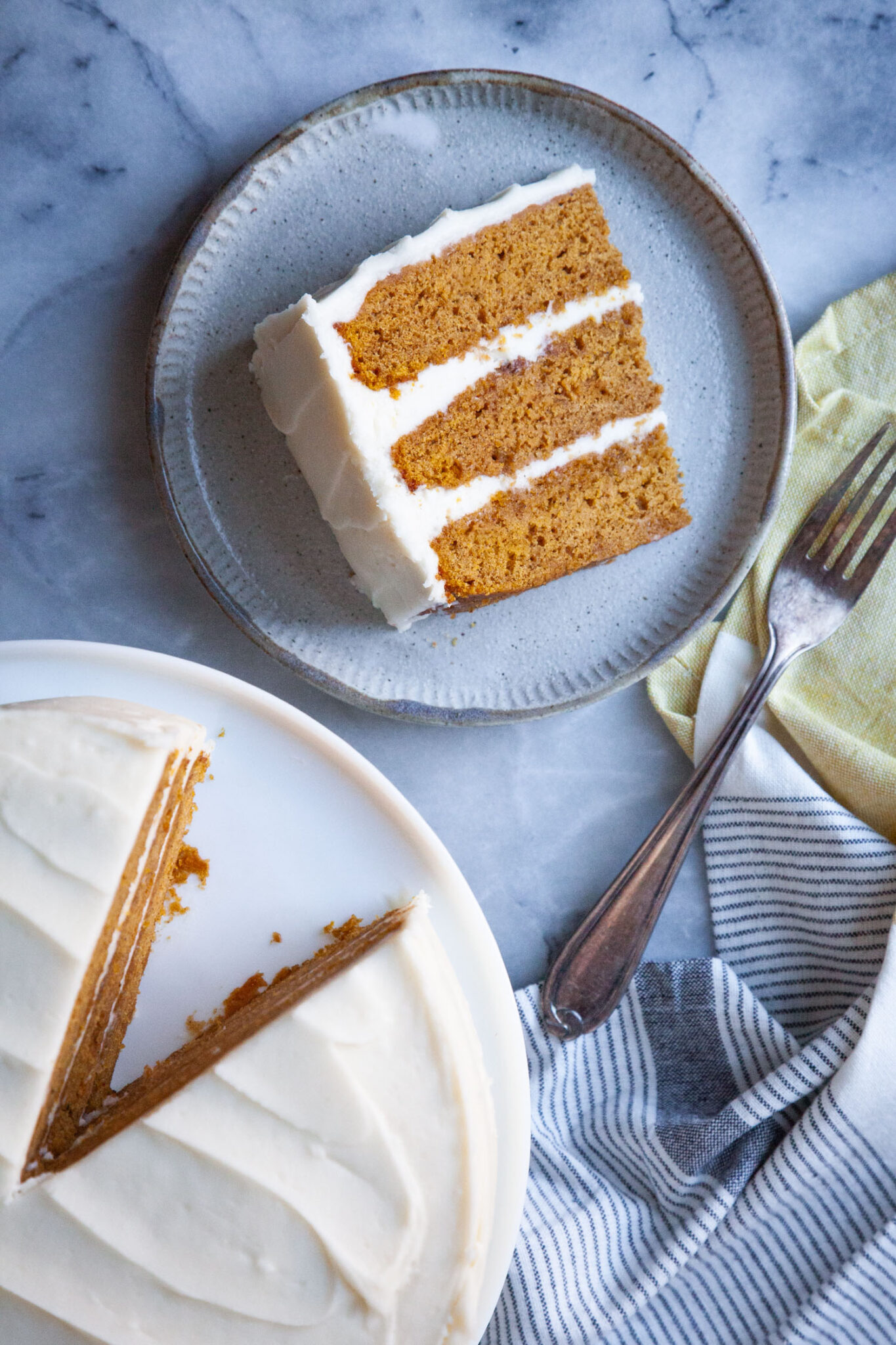 A slice of pumpkin layer cake on a plate, with the remaining cake on a cake stand next to it.