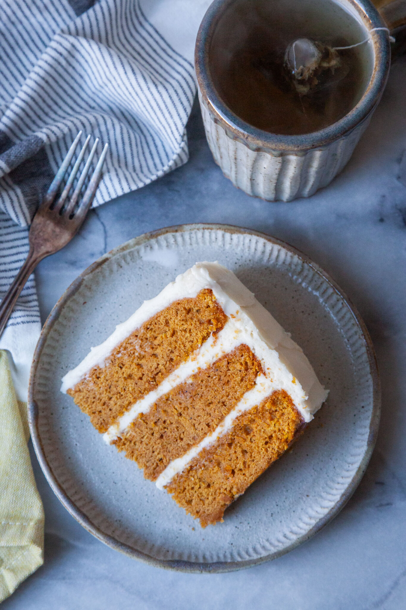 A slice of pumpkin layer cake on a plate, with a mug of tea next to it.