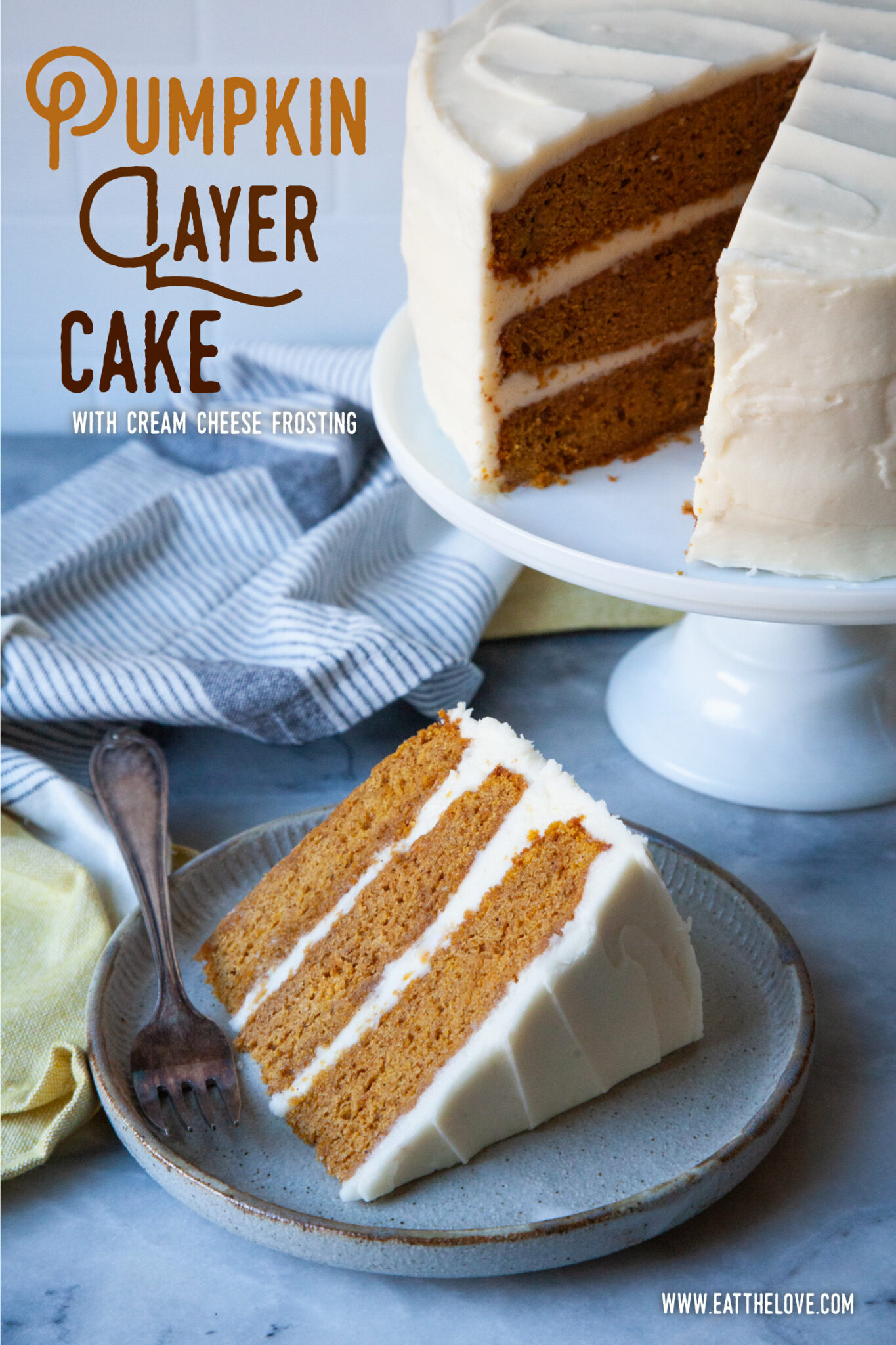 A slice of pumpkin layer cake with cream cheese frosting on a plate, with the remaining cake on a cake stand behind it. 