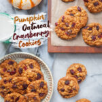 A plate of pumpkin oatmeal cranberry cookies, with more cookies on the table and on a cutting board. There is a glass of milk and a small decorative pumpkin next to the plate. The text on the image says pumpkin oatmeal cranberry cookies.