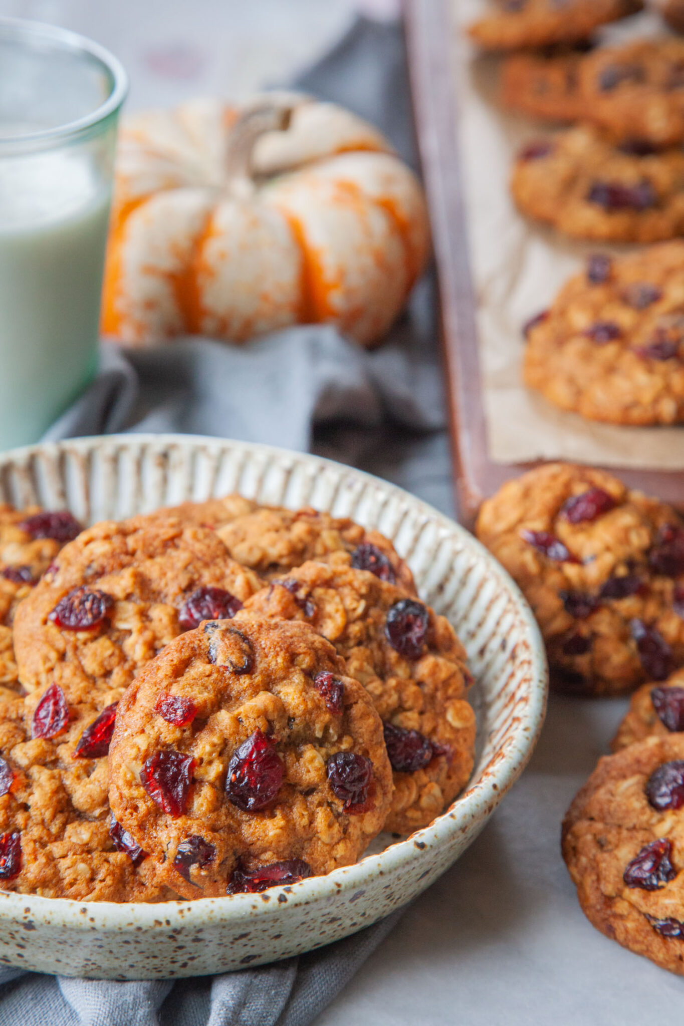 A plate of pumpkin oatmeal cranberry cookies with more cookies next to it, and a glass of milk behind it.