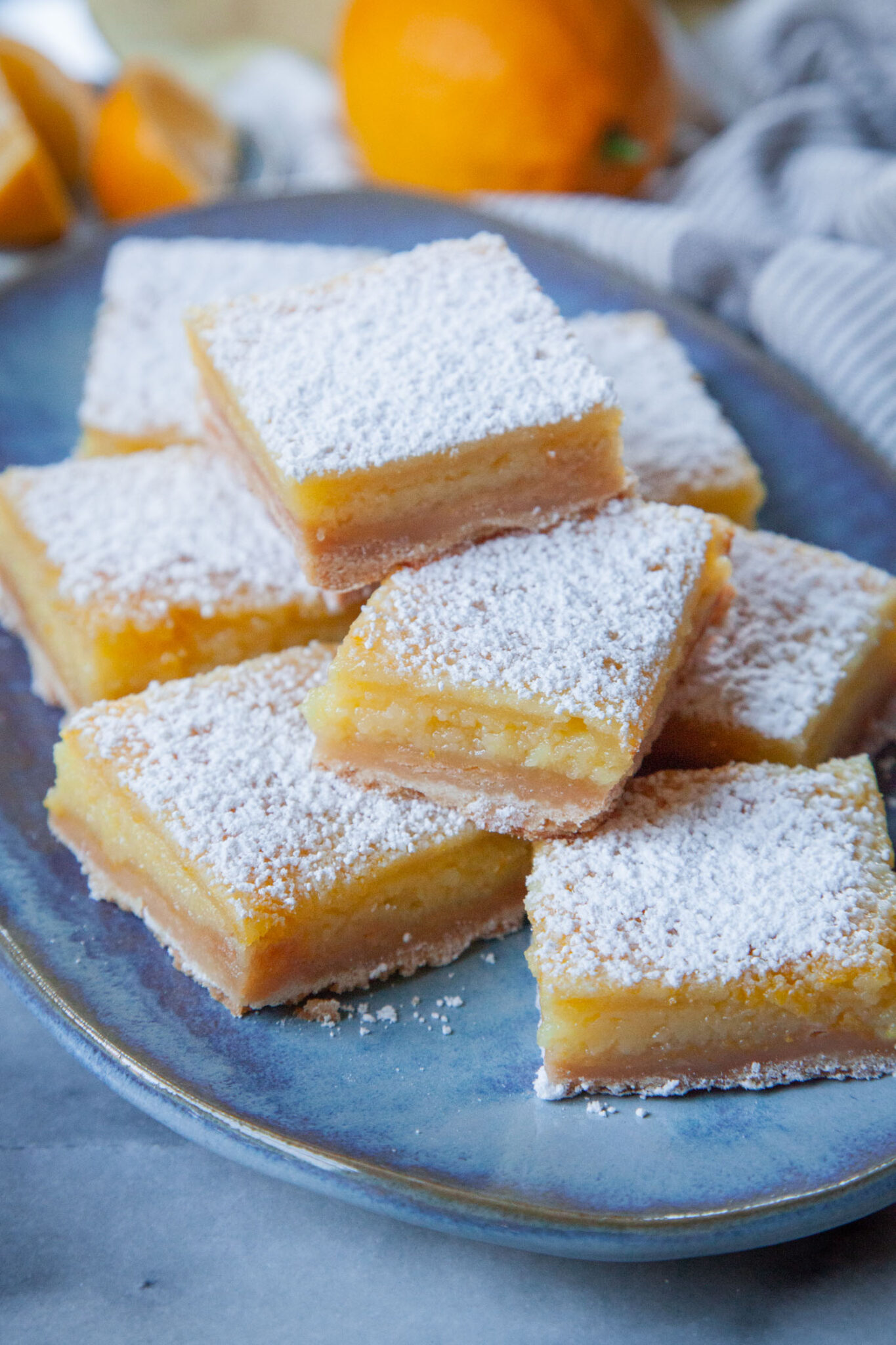 A stack of Meyer lemon bars on a blue plate, with a whole Meyer lemon behind the plate.
