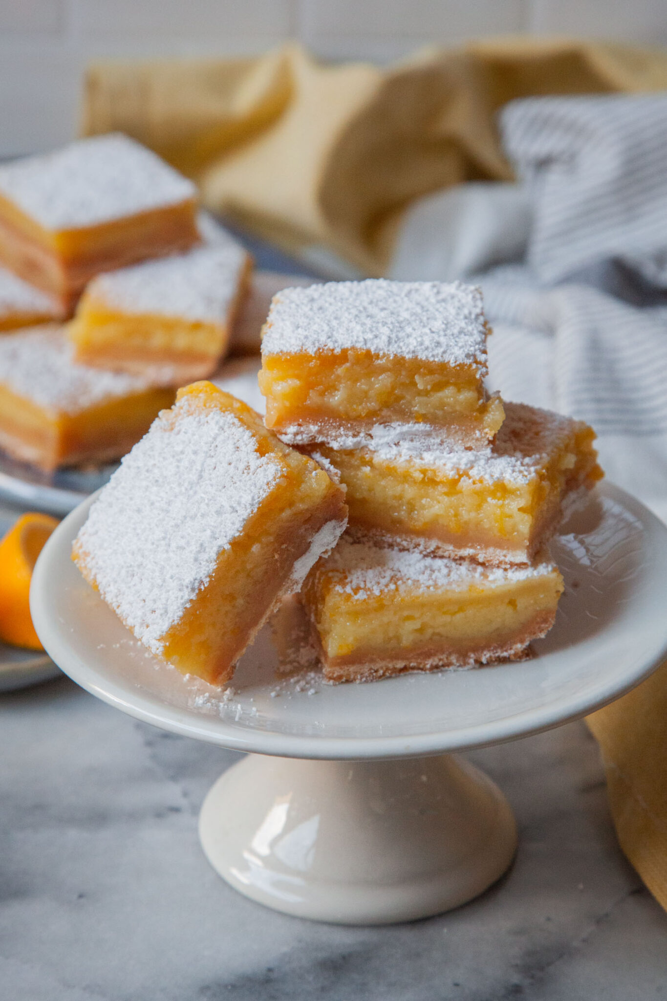 Meyer lemon bar on a small pedestal plate, with more Meyer lemon bars behind it.