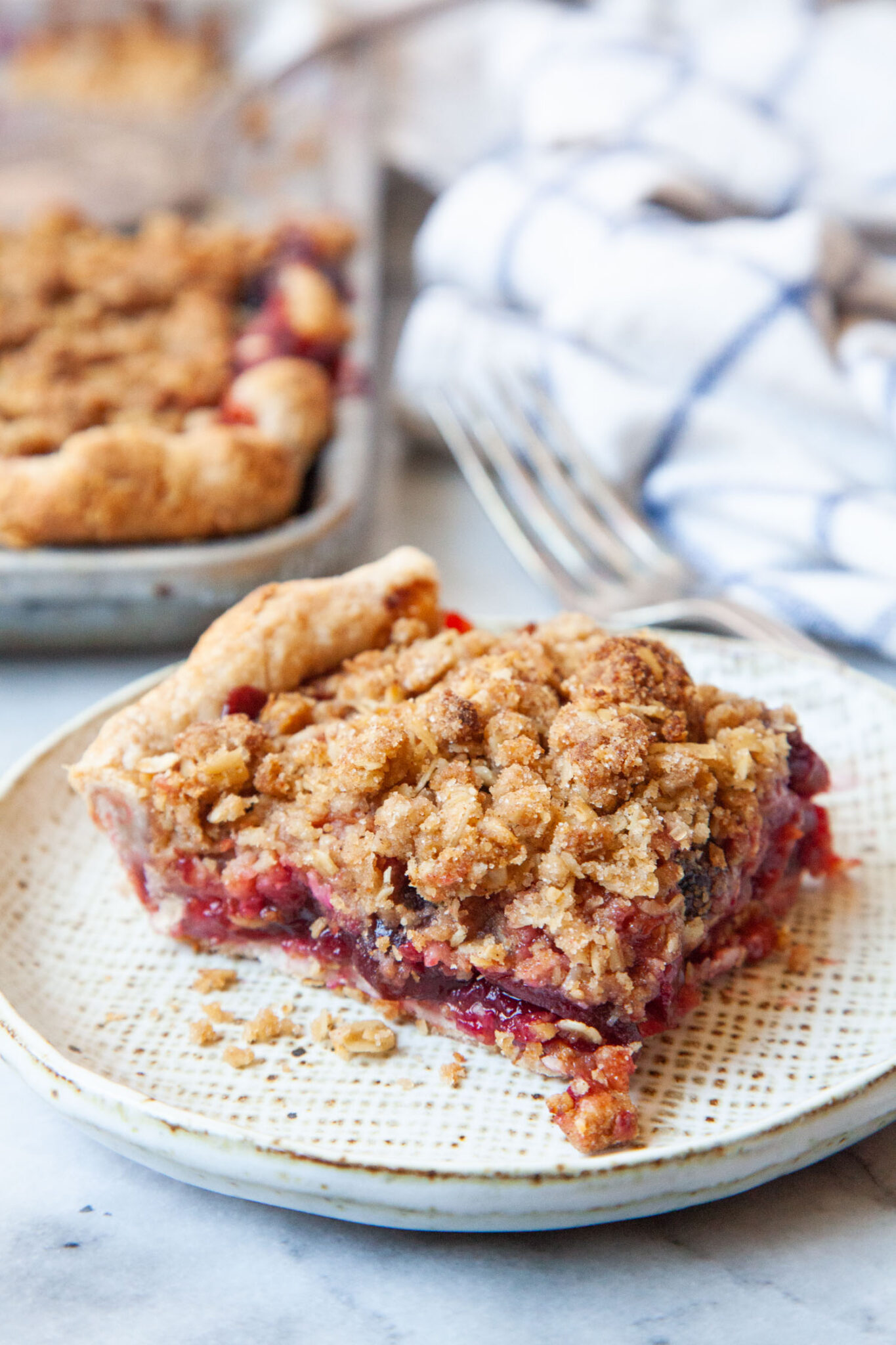 A slice of apricot cherry slab pie on a plate, with the remaining pie behind it.
