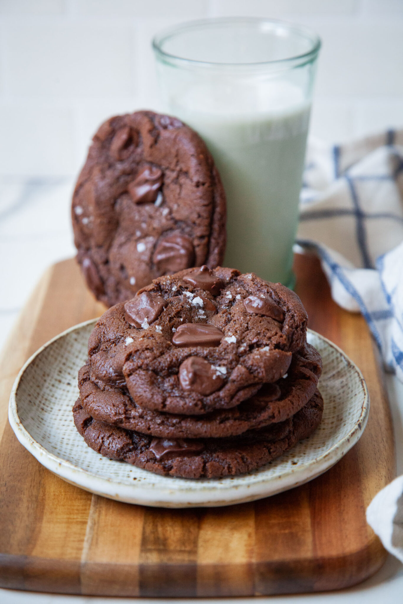 A plate of mocha chocolate chip cookies, with a glass of milk behind it. There is a cookie propped up against the glass.