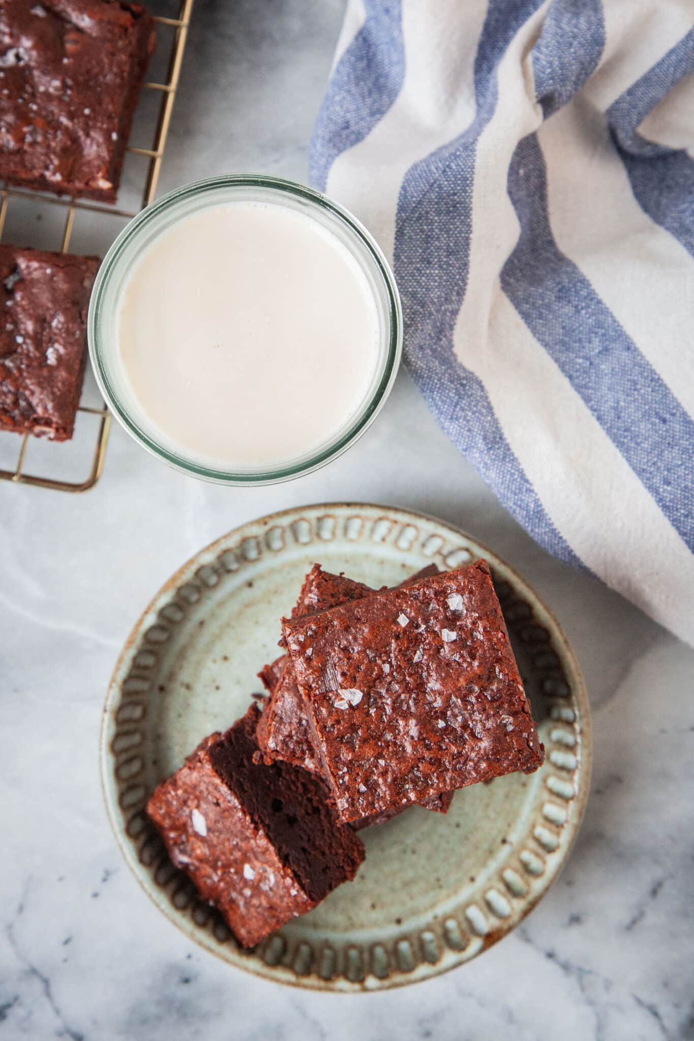 A plate of olive oil brownies with sea salt, with a glass of milk and more brownies next to it.