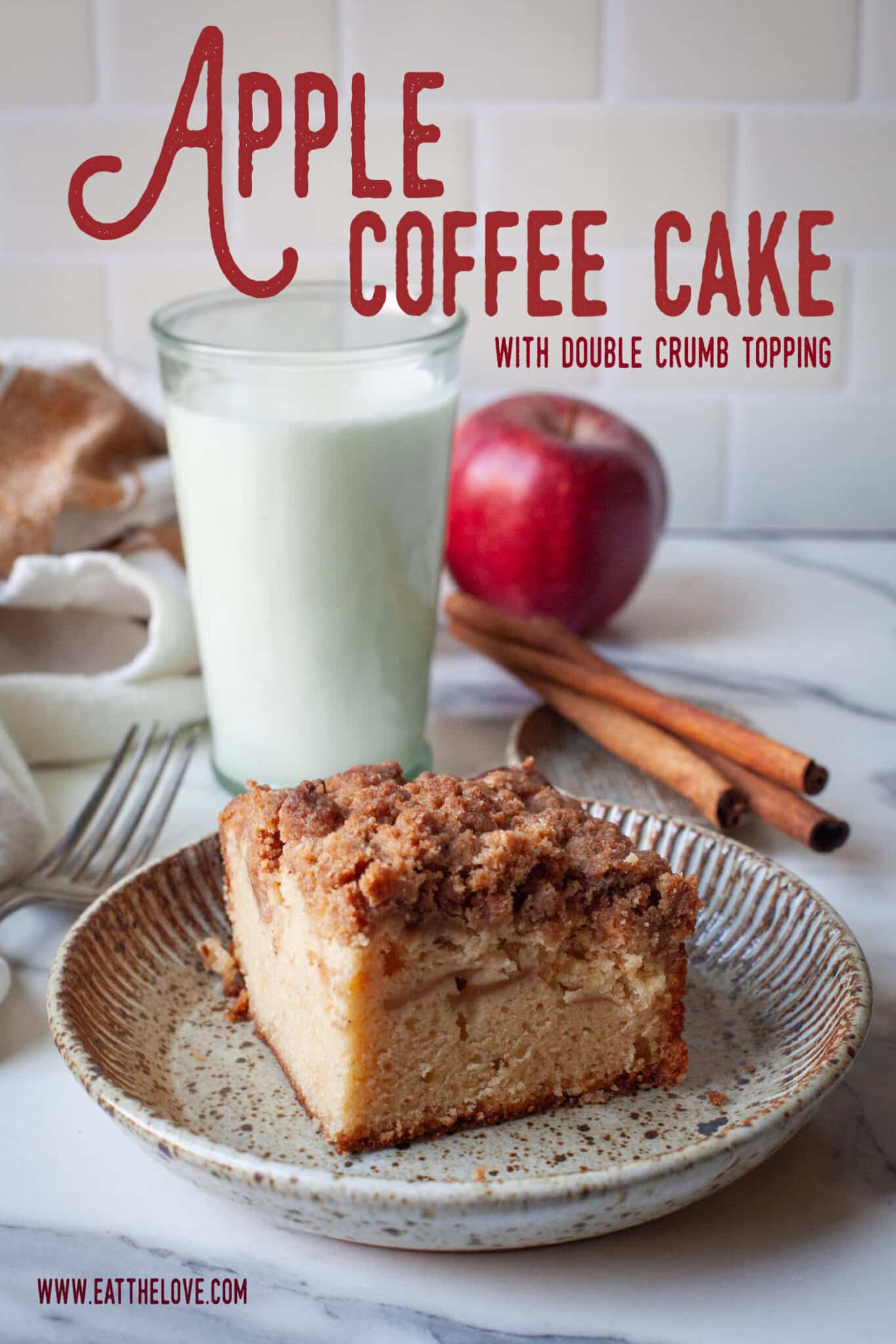 A slice of apple coffee cake on a plate, with a glass of milk, and apple and cinnamon sticks behind it.