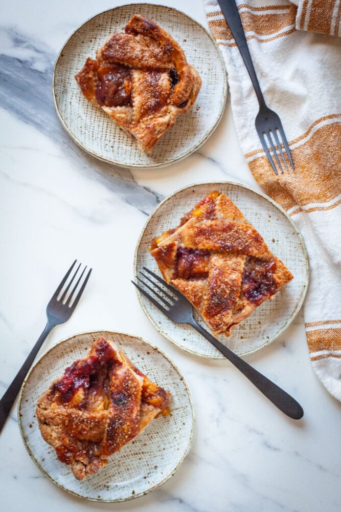 Three plates, each with a slice of peach and blackberry slab pie on them.