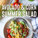 A bowl of avocado and corn salad, with an ear of corn, grape tomatoes, and a lime next to the bowl. The type on the image says Avocado and Corn Summer Salad.