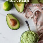 A scoop of avocado and lime ice cream in a glass cup, with a cut avocado and lime next to it.