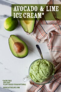 A scoop of avocado and lime ice cream in a glass cup, with a cut avocado and lime next to it.