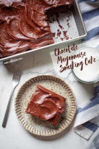 A slice of chocolate mayonnaise cake on a plate, with the remaining cake in a pan next to it.